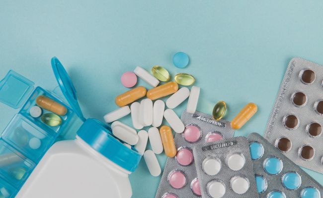 Zdjęcie przedstawia opakowania od leków i tabletki w różnych kolorach.