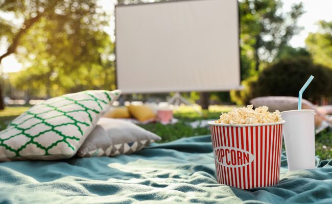 Zdjęcie przedstawia koc piknikowy i stojący na nim popkorn. W tle ekran dla rzutnika.